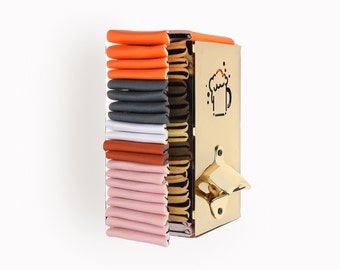 May include: A gold metal wall-mounted beer bottle opener with a built-in storage rack for multiple bottle caps. The rack is filled with colorful bottle caps in shades of orange, gray, white, brown, and pink.