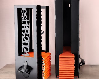Puede incluir: Porta latas de pared de metal negro con abridor de botellas integrado. El soporte tiene un letrero que dice "Est 1924" y está lleno de latas de bebidas naranjas.