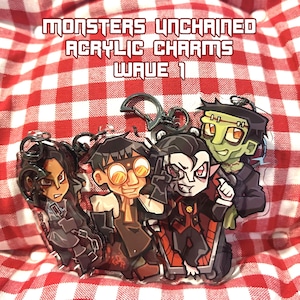 May include: Acrylic charm set featuring four cartoon monster characters. The charms have a glossy finish and are attached to silver-colored keychains. The text "MONSTERS UNCHAINED ACRYLIC CHARMS WAVE 1" is displayed in red block letters.