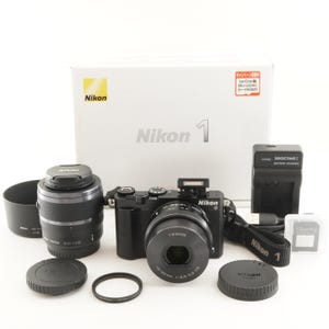 May include: A black Nikon 1 digital camera with a 10-30mm lens, an additional 30-110mm lens, a lens hood, two lens caps, a battery charger, a memory card, a camera strap, and the original white Nikon 1 product box with Japanese text labels.