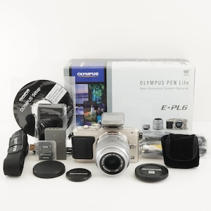 Könnte beinhalten: Silbernes Olympus PEN Lite E-PL6 Kamera-Kit mit Zubehör, darunter ein Objektiv, Blitz und Speicherkarte. Das Kit enthält einen schwarzen Kameragurt, Objektivdeckel und eine Box mit dem Olympus-Logo und Produktinformationen.