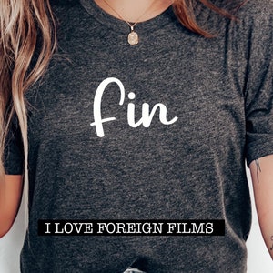 Op de afbeelding: Donkergrijs t-shirt met het woord "Fin" in witte letters. Onder het woord "Fin" staat de tekst "I LOVE FOREIGN FILMS" in een zwarte rechthoek. Het t-shirt heeft een ronde hals.