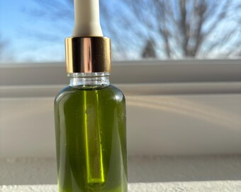 May include: A glass bottle with a gold lid and a white dropper. The bottle is filled with a green liquid.