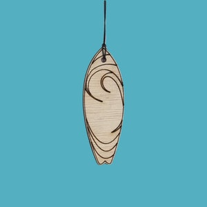 May include: A wooden surfboard-shaped ornament with a black string for hanging. The light-coloured wood has a grain pattern and is decorated with black wave designs. The background is a solid teal colour.