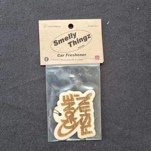 May include: A wooden car air freshener with the words "Fishin' Cone" cut out. The freshener is in a clear plastic bag, with a cardboard backing that reads "Smelly Thingz Australia" and "Car Freshener". The background is a dark grey fabric.