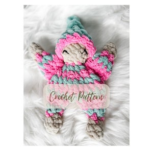 May include: A crocheted plush toy in the shape of a person wearing a pink and teal striped outfit. The toy has a beige face with embroidered eyes and a small mouth. The text "Crochet Pattern" is visible in the image.