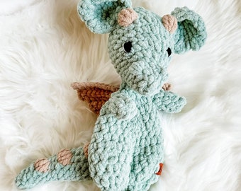May include: A crocheted green dragon toy with brown accents. The dragon has a long tail, wings, and a friendly face.