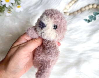 Peut inclure: Un petit animal en peluche violet et blanc avec un visage mignon. L'animal est tenu dans une main.
