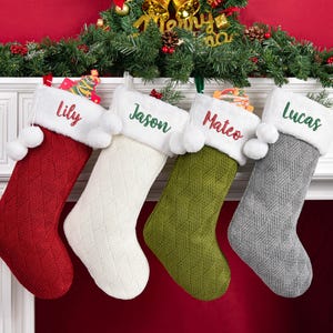 Peut inclure: Quatre bas de Noël personnalisés, rouges, blancs, verts et gris, avec un nom brodé sur le revers blanc. Les bas sont suspendus à une cheminée blanche, décorée de verdure festive.