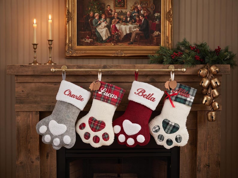 May include: Four paw-shaped Christmas stockings hanging on a rod. The first is gray with a white cuff and paw pad. The second is white with a red plaid cuff and paw pad. The third is red with a white cuff and paw pad. The fourth is white with a green plaid cuff and paw pad. Each features embroidered names: Charlie, Lucas, Bella, and Olivia.