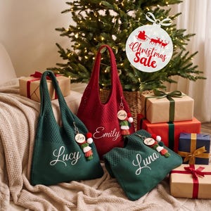 May include: Three knit tote bags in dark green and deep red, each featuring a personalized name in white script: Lucy, Emily, and Luna. Each bag includes a decorative wooden keychain with a colorful tassel. The bags are arranged with gift boxes.