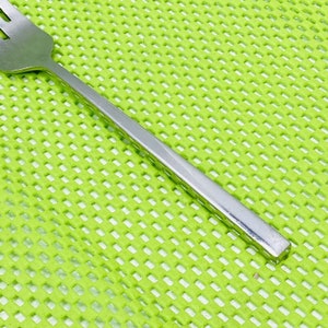 May include: A silver fork with a textured handle. The fork is lying on a green placemat.