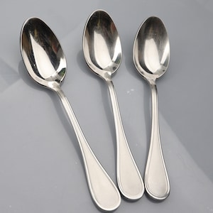 Puede incluir: Tres cucharas de plata con cuencos redondeados y mangos largos y delgados. Las cucharas están dispuestas en fila, con los mangos apuntando hacia la derecha.