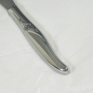 Pode incluir: Uma faca de manteiga de prata com um design floral no cabo.