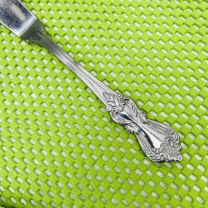 以下が含まれることがあります： 装飾的なハンドルが付いた銀製のバターナイフ。ハンドルは花柄で、光沢のある仕上げになっています。