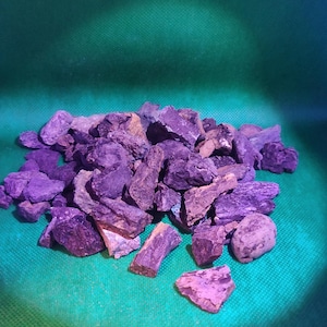 May include: A pile of rough, irregularly shaped rocks in shades of purple and brown. The rocks are scattered on a green surface, with a gradient of blue in the background. The lighting creates shadows and highlights on the rocks.