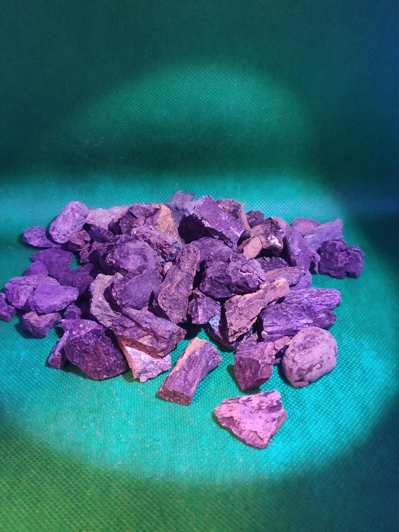 May include: A pile of rough, irregularly shaped rocks in shades of purple and brown. The rocks are scattered on a green surface, with a gradient of blue in the background. The lighting creates shadows and highlights on the rocks.
