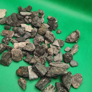 May include: A collection of various-sized, dark gray and brown rocks scattered on a bright green surface. The rocks have rough, textured surfaces and irregular shapes, suggesting they are natural stones or minerals.