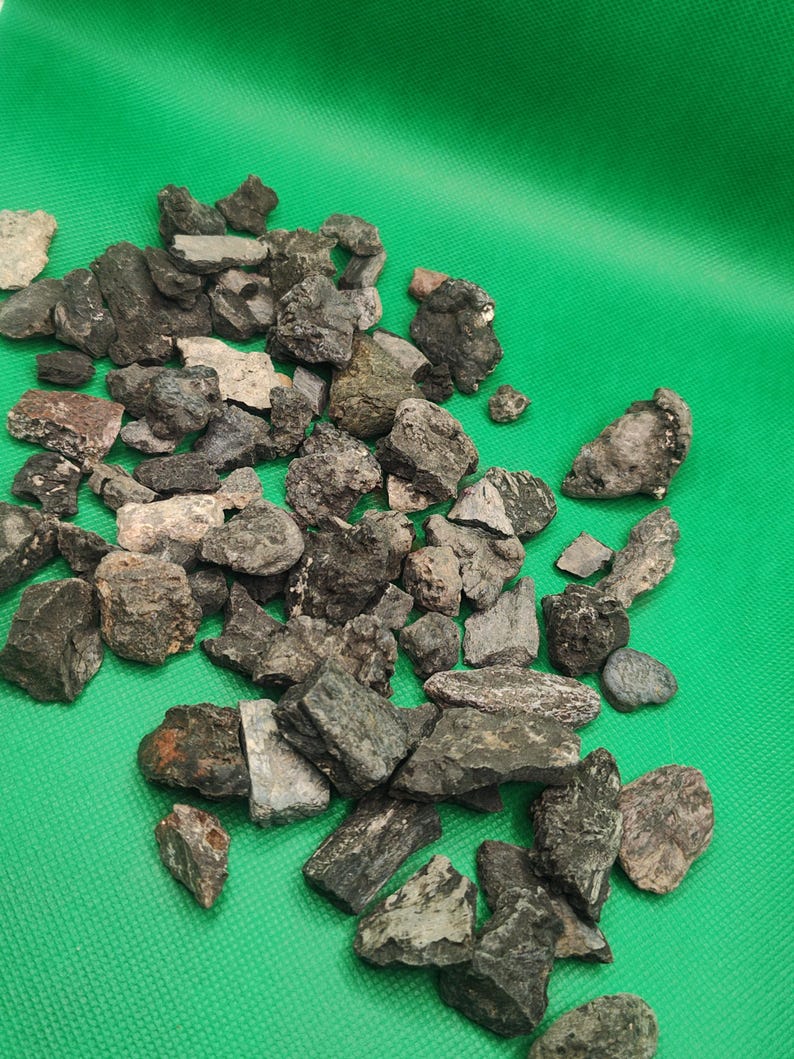 May include: A collection of various-sized, dark gray and brown rocks scattered on a bright green surface. The rocks have rough, textured surfaces and irregular shapes, suggesting they are natural stones or minerals.