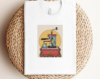May include: A white t-shirt with a vintage illustration of a coffee maker with a red and gold base and a blue and white coffee maker. The coffee maker is pouring coffee into two cups. The illustration is set against a yellow background with a sun.
