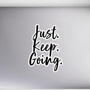Op de afbeelding: Een laptop met een zwart-witte sticker met de tekst "Just. Keep. Going."