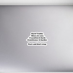 May include: A white sticker on a laptop with the text "Hard Truths: -Ideas are easy. Execution is hard. Consistency is harder. Start and don't stop." The sticker is surrounded by a notebook, pencils, headphones, a mouse, and a plant.