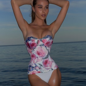 May include: A white strapless corset with a floral print featuring pink, blue, and white flowers. The corset is worn by a person standing in the water.