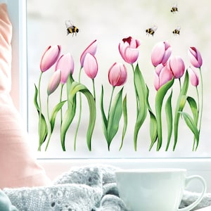 Könnte beinhalten: Ein Fensteraufkleber mit rosa Tulpen mit grünen Blättern und mehreren fliegenden Bienen. Das florale Design ist vor einem weißen Hintergrund platziert und schafft ein Frühlings- oder Gartenthema. Eine weiße Tasse und ein rosa Kissen befinden sich im Vordergrund.
