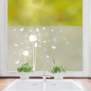 Könnte beinhalten: Weiße Fensteraufkleber mit Pusteblumen- und Schmetterlingsmotiven. Die Aufkleber sind auf einem Fenster angebracht, wobei ein verschwommener grüner Hintergrund durch das Glas sichtbar ist. Das Design umfasst mehrere Schmetterlinge und Pusteblumen.