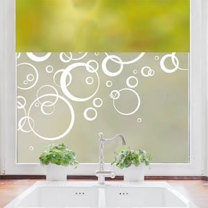 Könnte beinhalten: Ein Küchenfenster mit weißem Rahmen und einem Design aus sich überlappenden weißen Kreisen auf Milchglas. Unter dem Fenster befinden sich ein weißes Doppelwaschbecken, eine Chromarmatur und zwei Topfpflanzen.