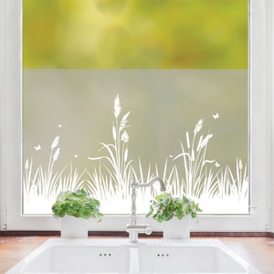 Könnte beinhalten: Weiße, gefrostete Fensterfolie mit einem Design aus hohem Gras und Schmetterlingen. Die Folie ist an einem Fenster in einer Küche mit Spüle und Wasserhahn angebracht.