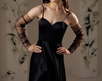 May include: A floor-length black satin dress with a sweetheart neckline, thin spaghetti straps, and a high side slit. The dress is paired with sheer, long black mesh gloves featuring small, evenly spaced dark embellishments along the fabric.