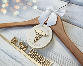 May include: A wooden hanger with a white ribbon and a circular tag featuring a medical symbol and the text "Louisiana State University" and "June 20, 2024". Below is a gold nameplate that reads "DR. PAUL RAMIREZ".