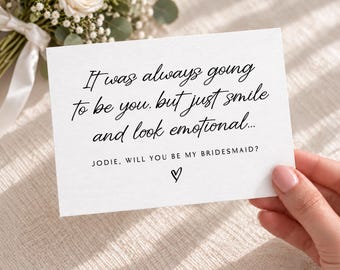 May include: A white rectangular card featuring black printed text that reads: It was always going to be you. but just smile and look emotional... JODIE, WILL YOU BE MY BRIDESMAID? with a small hand-drawn heart symbol centered at the bottom.
