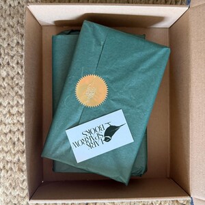 May include: A brown cardboard box with a green tissue paper wrapped package inside. The package has a gold seal and a business card that says "Lark Sparrow Books".