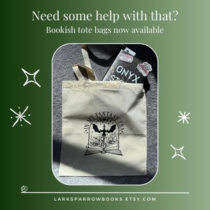 May include: A beige tote bag with a black design that says "In My Fantasy Era" with a crescent moon, stars, and a bat. The bag is filled with a book with the title "Onyx Stars" and a sticker.