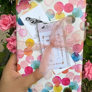 May include: A wrapped book with a pink and white polka dot pattern. The book is tied with a pink ribbon and has a small card attached to it with a bird illustration and the text "Mark Sparrow Books".