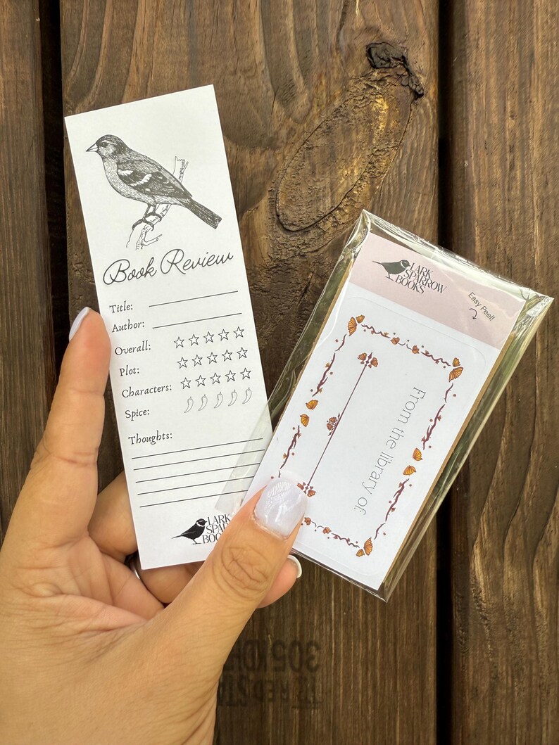 May include: A white bookmark with a black and white illustration of a bird. The bookmark has a section for a book review with headings for title, author, overall, plot, characters, spice, and thoughts. The bookmark also has a section for rating the book with stars and chili peppers.