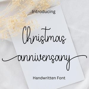 Può includere: Una carta bianca con le parole "Christmas anniversary" in un carattere scritto a mano. Sono presenti anche le parole "Introducing" e "Handwritten Font". Fiori secchi nell'angolo in alto a sinistra.