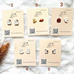 May include: Five cards with different pairs of earrings on them. The earrings are made of titanium and have a variety of designs, including ghosts, coffee cups, pumpkin, and pie. Each card has a QR code and the text "Scan to connect with me".
