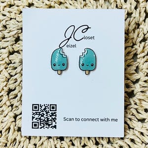 May include: A pair of blue popsicle earrings with a bite taken out of each. The earrings are on a white card with the text "JC closet eizel" and a QR code. The card also says "Scan to connect with me."