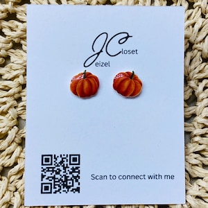 May include: A pair of pumpkin-shaped stud earrings. The earrings are orange and have a glossy finish. The earrings are displayed on a white card with the text "JCloset eizel" and a QR code with the text "Scan to connect with me".