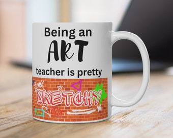 May include: White ceramic mug with black text that reads "Being an ART teacher is pretty SKETCHY". The text is on a white background with a brick wall pattern at the bottom of the mug.