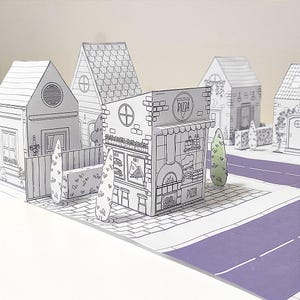 May include: A pop-up paper town scene featuring a pizza shop and several houses. The buildings are outlined in black and white, with a purple road and green trees. The pizza shop has a sign that says "Pizza".