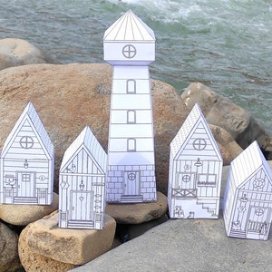 Könnte beinhalten: Fünf Papierhäuser, darunter ein Leuchtturm, mit schwarzen Umrissen und Details auf weißem Hintergrund. Die Häuser sind auf Felsen in der Nähe eines Flusses angeordnet.