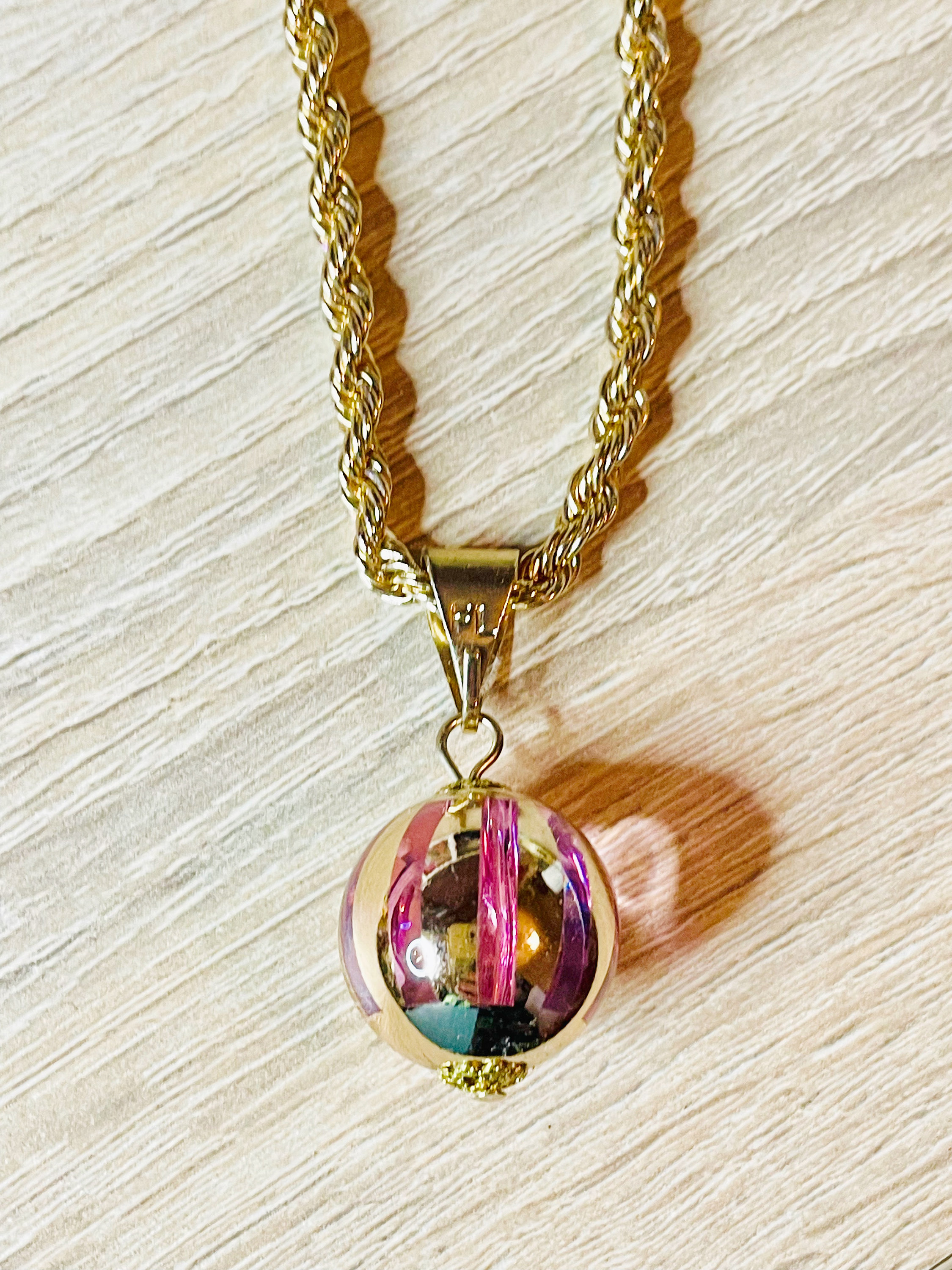 Puede incluir: Un collar de cadena de oro con un colgante redondo de vidrio multicolor. El colgante tiene un patrón de espiral y está unido a la cadena con un cierre de oro.