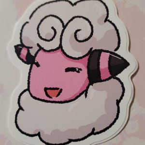May include: A pink and white cartoon sheep with a happy expression. The sheep has a fluffy white coat and a pink face with black eyes and a black nose. The sheep is smiling and has its tongue sticking out.