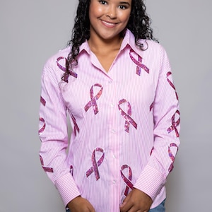 Può includere: Camicia a righe rosa e bianche con maniche lunghe. La camicia presenta diversi motivi a nastro rosa con paillettes. La camicia è realizzata in un tessuto leggero ed è adatta per l'uso quotidiano.
