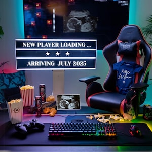 Puede incluir: Una configuración de juego con una silla de juego negra, un teclado, un mando y un cartel que dice "Nuevo jugador cargando... Llegando en julio de 2025".