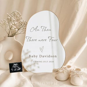 Peut inclure: Annonce de grossesse avec un miroir blanc en forme abstraite portant l'inscription "An Then There were Four" et "Baby Davidson COMING JULY 2026". L'image comprend un vase avec des fleurs, des chaussons de bébé et une échographie.